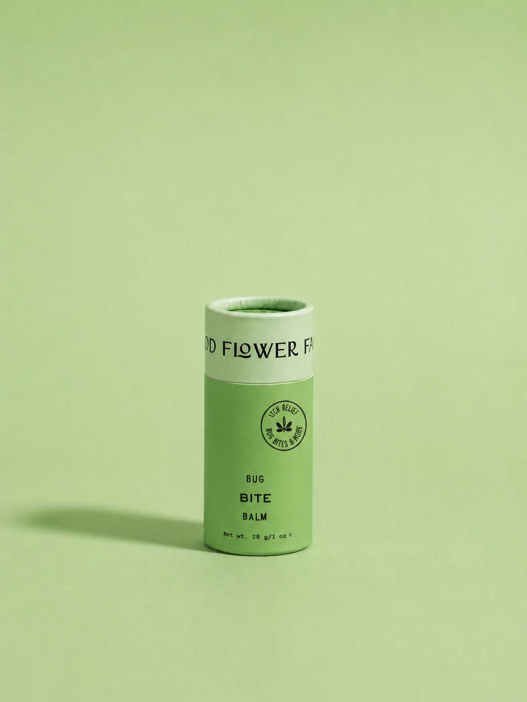 A green cylindrical container labeled “Bug Bite Balm For Anti-Itch” by Good Flower Farm stands upright on a light green background. The label features a small leaf icon.