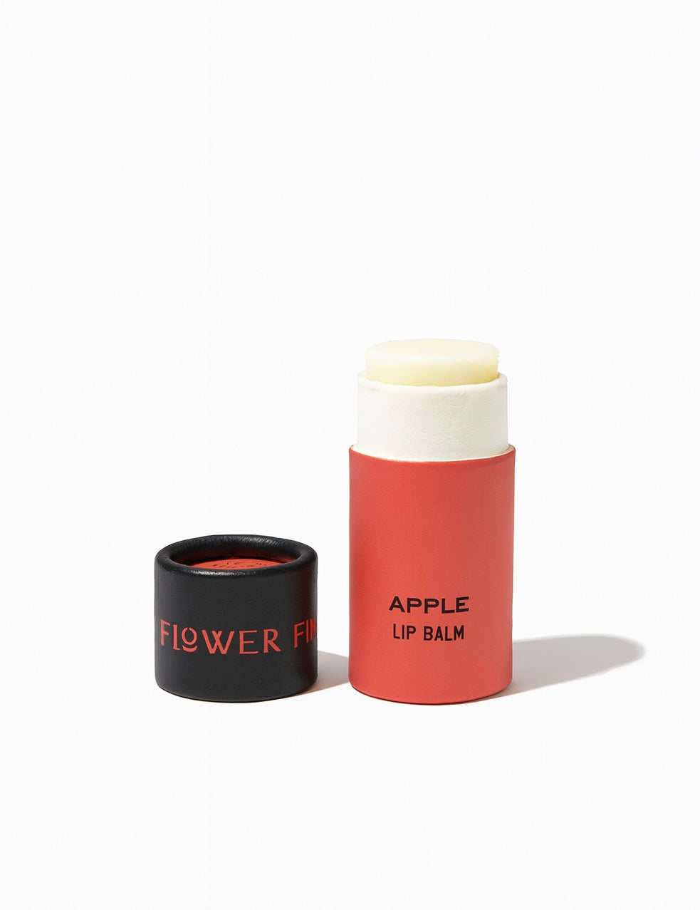 A red tube of SEASONAL LIMITED Apple Organic Lip Balm by Good Flower Farm with the cap off, revealing the balm inside. The black cap has FLOWER in red, and APPLE LIP BALM is printed on the tube. Background is white.
