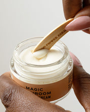 A hand holds a jar of cream as another uses a Good Flower Farm Reusable Bamboo Spatula (from the Set of 5) to scoop some out.