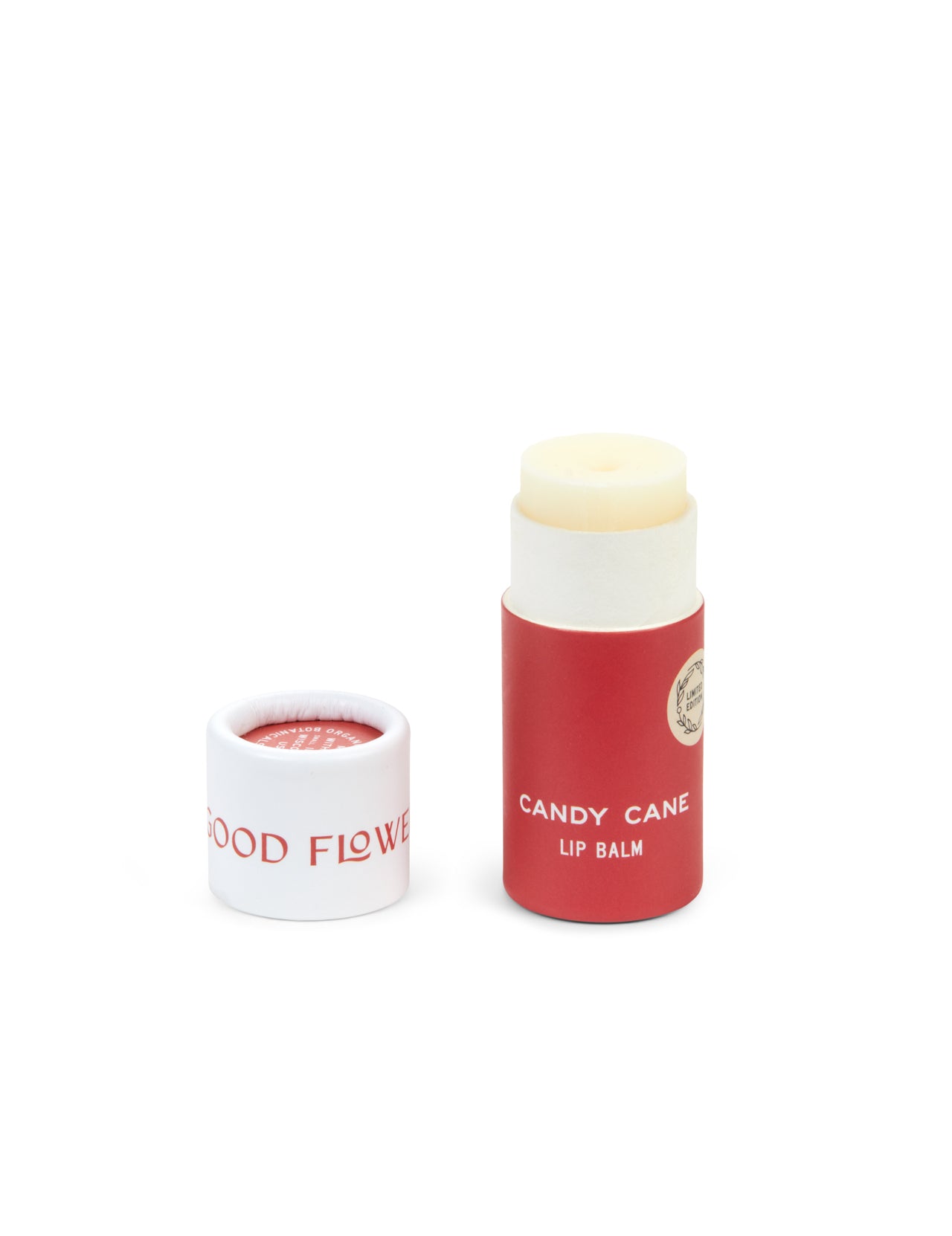 A red and white cylindrical tube of SEASONAL LIMITED Holiday Lip Gift Set - NEW by Good Flower Farm stands next to its removed cap. The eco-friendly, biodegradable packaging contains light-hued lip balm made with coconut oil.