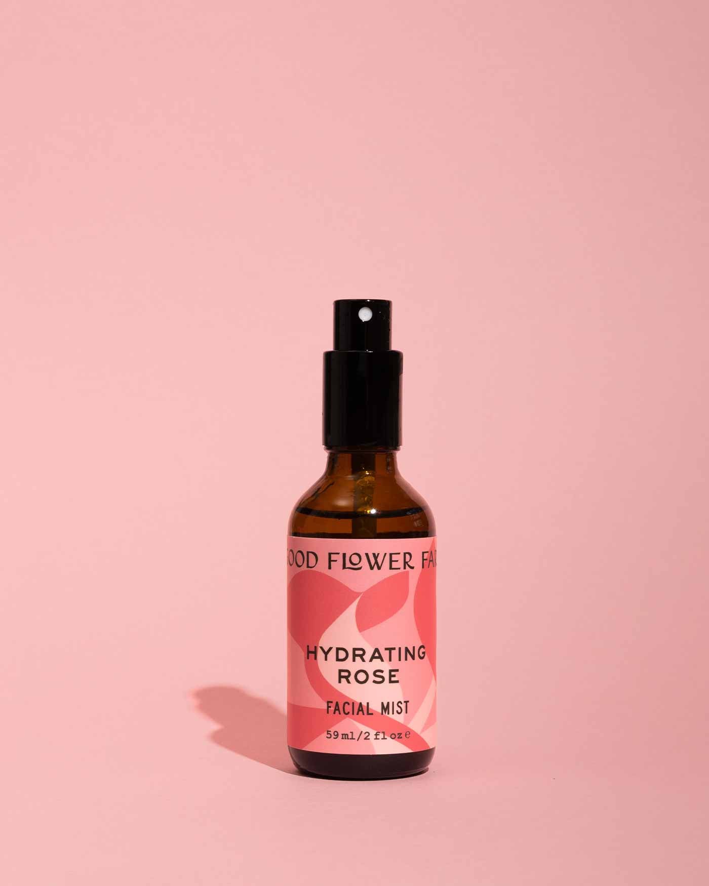 A brown glass spray bottle from good-flower-farm’s Dry Skin Bundle: Save 15% is displayed upright on a pink surface against a matching pink background. The label—adorned with abstract pink shapes and black text—suggests facial moisturizing benefits, making it an ideal choice for soothing and refreshing dry skin.