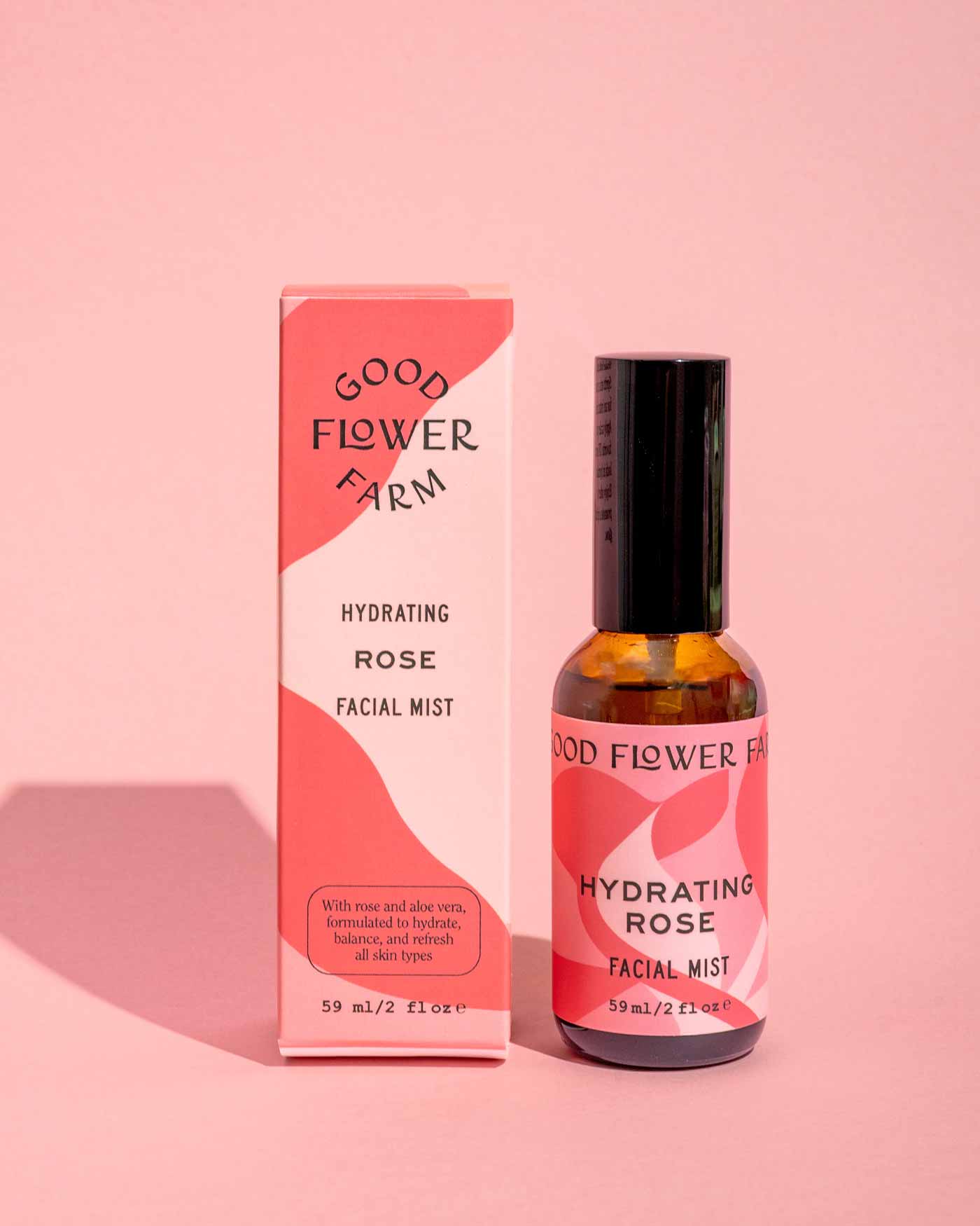 A bottle and box from the Good Flower Farm Dry Skin Bundle: Save 15% feature pink, red, and white abstract designs as they rest on a pink background. Perfect for facial moisturizing and ideal for dry skin.