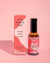 A bottle and box from the Good Flower Farm Dry Skin Bundle: Save 15% feature pink, red, and white abstract designs as they rest on a pink background. Perfect for facial moisturizing and ideal for dry skin.