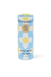 A cylindrical Good Flower Farm Good Baby Gift Set container sits on a blue background with white, yellow-centered flowers. Its label displays a gold emblem and black text, highlighting gentle botanical ingredients.