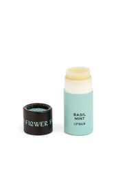 A Rainbow Organic Lip Balm from Good Flower Farm, shown in a light blue biodegradable wrapper with its black cap off and beside it on a white background; this is one of six balms in the set.